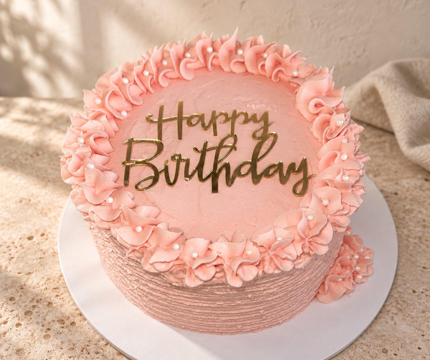 Pink buttercream birthday cake with piped decoration and gold lettering